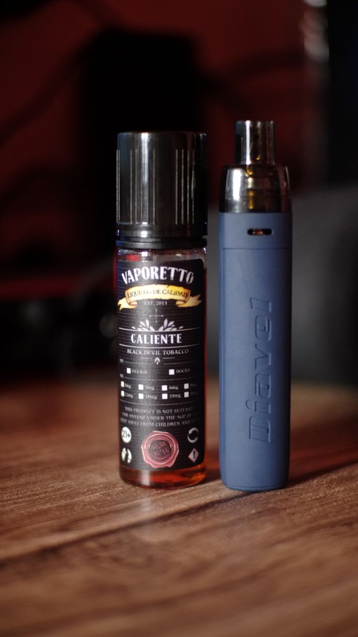 A close-up of Vaporetto e-liquid bottle and Diavel vape against a dark backdrop on a wooden table.