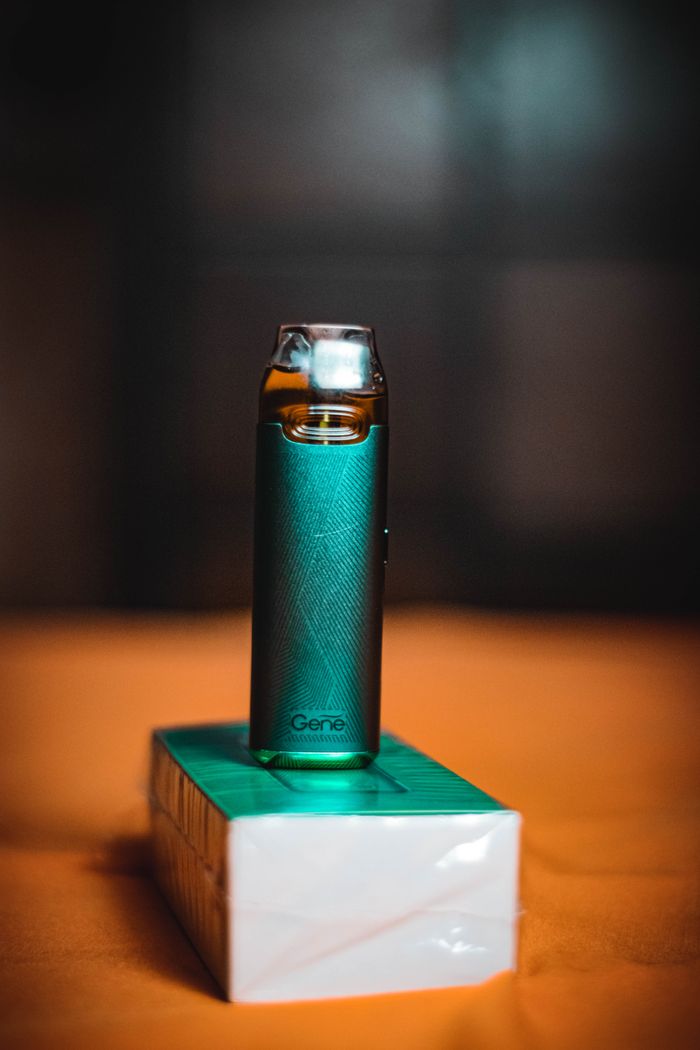 A stylish green vape device resting on a box, captured with soft lighting and a blurred background.